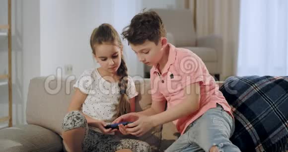 大哥哥和小妹妹放学后有一段时间在一起他们坐在沙发上拿着智能手机玩视频的预览图