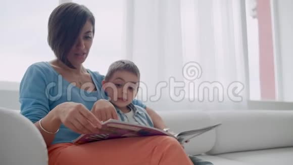 快乐的母子儿子在床上笑着看书幸福的家庭母亲和孩子儿子读着躺着的书视频的预览图
