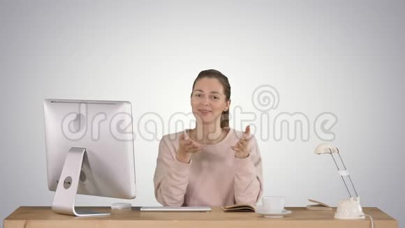 微笑着的千禧一代女人坐在办公桌前对着镜头微笑在渐变的背景下交谈视频的预览图