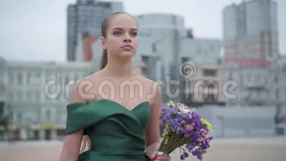 美丽的女孩穿着别致的裙子站在清晨城市的背景上散发着芬芳的野花实际视频的预览图