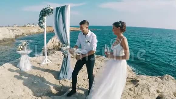 生活方式视频新婚快乐的新婚夫妇在海边的一块岩石上庆祝婚礼溅上香槟视频的预览图