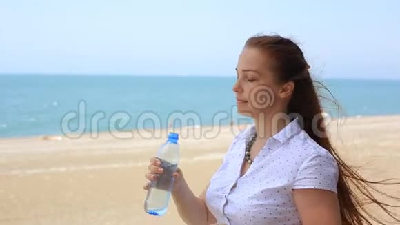 女人从海滩上的瓶子里喝水视频的预览图