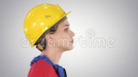 年轻的女工程师带着黄色的安全帽在梯度背景上行走和微笑视频的预览图
