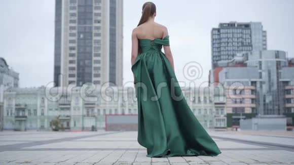 美丽美丽美丽的女孩穿着一件漂亮的晚绿色连衣裙迷人地走在附近空荡荡的城市广场上视频的预览图