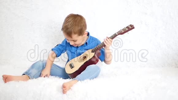 欢快的男孩坐在白色的沙发上慢动作地弹着一儿童的吉他视频的预览图