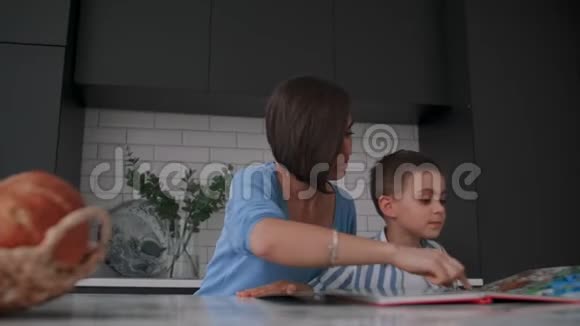 一位年轻的西班牙母亲和她的儿子坐在桌子旁教他读孩子帮助和鼓励他的儿子视频的预览图