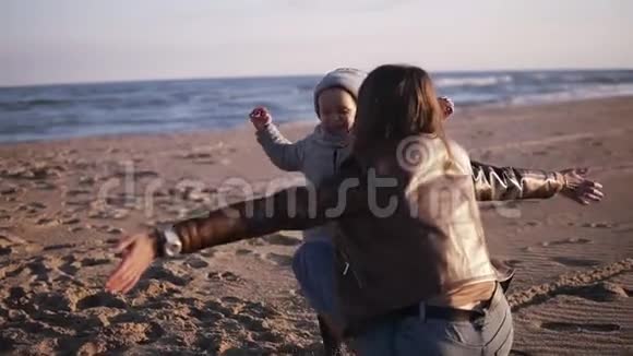 快乐的母亲在秋天的海滩上拥抱她的孩子可爱的孩子抱着他妈妈他们摔倒在沙子上概念视频的预览图