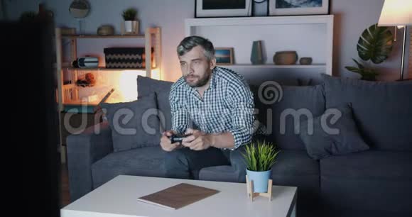 留胡子的家伙晚上在家玩电子游戏沙发上拿着操纵杆视频的预览图