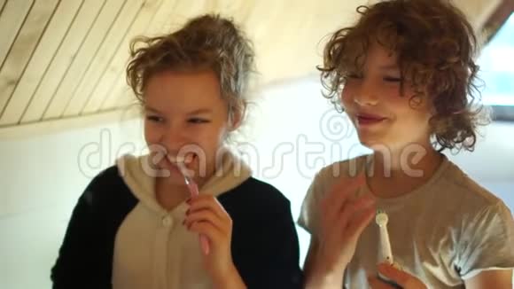 男孩使用电动牙刷兄妹俩在镜子对面的浴室里刷牙牙科视频的预览图