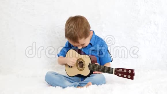 快乐的男孩坐在白色的沙发上弹着儿童的吉他视频的预览图