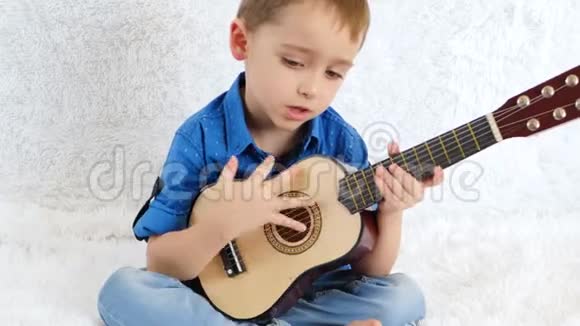 男孩坐在白色的沙发上弹着一儿童的吉他视频的预览图