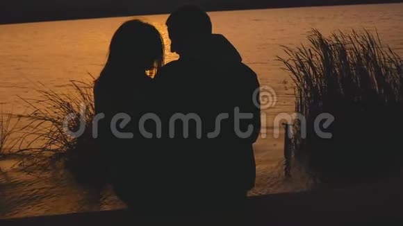 美丽的剪影浪漫夫妇休息在爱抚在黄昏湖视频的预览图