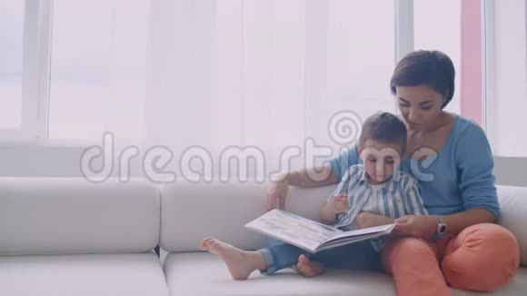 快乐的母子儿子在床上笑着看书幸福的家庭母亲和孩子儿子读着躺着的书视频的预览图