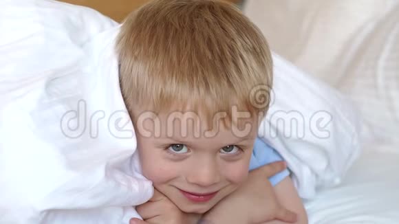 特写一个小蓝眼睛男孩的脸在一张白色毯子下的床上视频的预览图