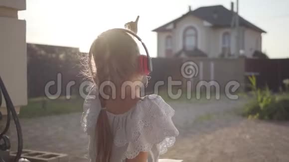 一个戴着耳机的漂亮可爱的小女孩坐在门廊上挥舞着挥舞着双手孩子视频的预览图