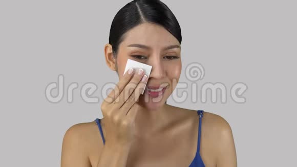 微笑的亚洲女孩从颧骨上脱妆湿擦穿着蓝色的顶级美容概念复制空间视频的预览图
