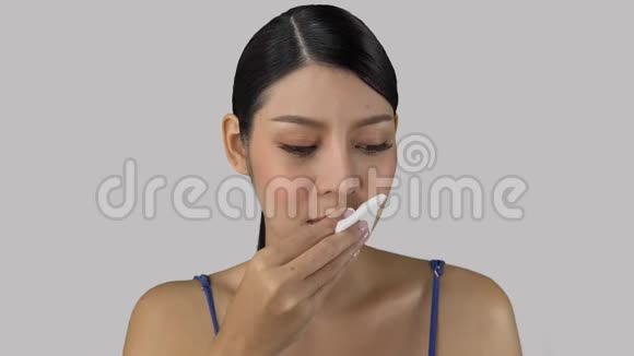 亚洲女孩用湿巾清洁嘴唇摆着灰色的化妆概念视频的预览图