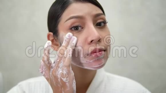 年轻微笑的东方女人在她的浴室里洗她的脸在镜子前美丽的夜晚视频的预览图