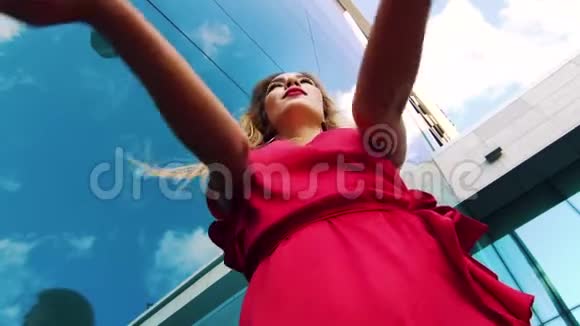 低角度拍摄的性感金发女人穿着红色裙子与摩天大楼跳舞视频的预览图