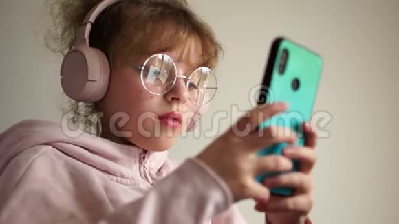 女学生用耳机和智能手机听音乐戴眼镜的女孩亲密肖像视频的预览图