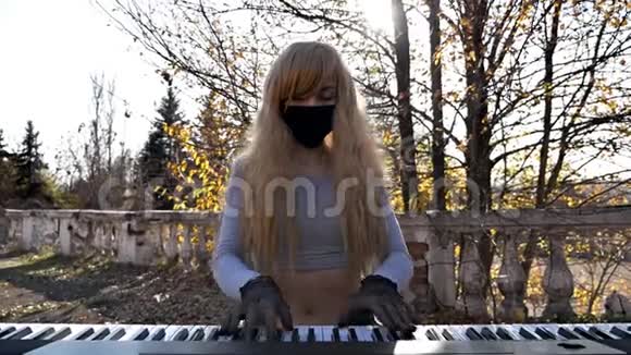 在一个秋天的公园里戴着黑手套戴着面具的金发女子在一个合成器上玩耍视频的预览图