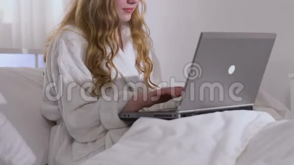 女士穿着浴袍在笔记本电脑上打字下班后在家放松聊天视频的预览图