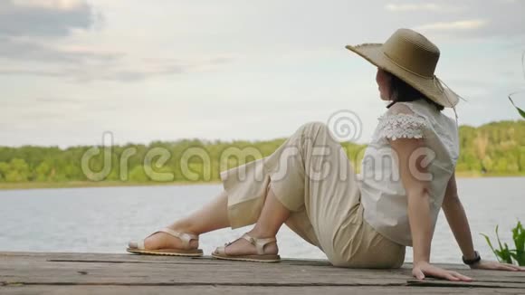 女孩坐在一个古老的木制码头码头码头的边缘视频的预览图