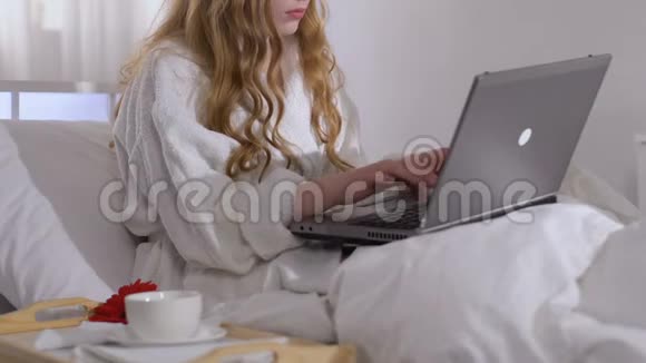 商务旅行期间女士在酒店客房内喝咖啡和工作笔记本电脑视频的预览图