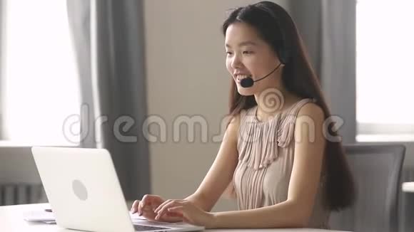 亚洲女商人接待员戴耳机手提电脑咨询客户视频的预览图