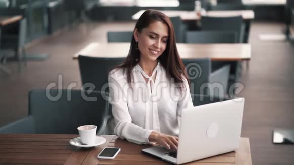 漂亮的女商人用智能手机和笔记本电脑在咖啡馆工作慢动作视频的预览图