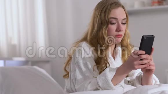 在床上哭泣的女人在智能手机上打字和男朋友吵架视频的预览图