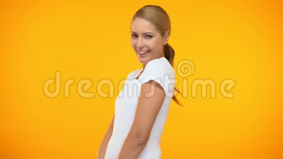 迷人的女人在橙色背景下跳舞眨眼相机调情女性气质视频的预览图