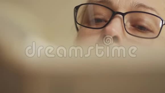 一个女人翻阅一本书的特写戴着眼镜的金发女人在看书视频的预览图