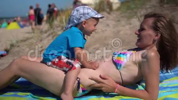 穿泳衣的漂亮女人和她的小男孩在海滩可爱的妈妈和她的儿子视频的预览图