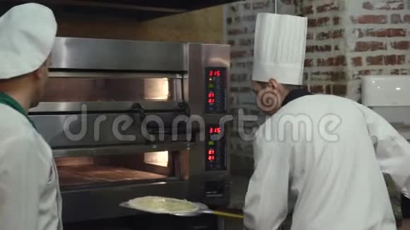 两位厨师将生披萨放入热比萨饼烤箱视频的预览图