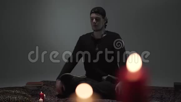 年轻的臀部坐着闭着眼睛盘腿在一个空房间里蜡烛冥想灵性魔力视频的预览图