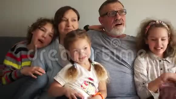 一个幸福的大家庭的亲密肖像祖父母正坐在沙发上拥抱他们的三个孙子家庭视频的预览图