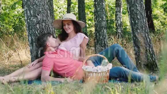 野餐时间快乐的年轻夫妇接吻男人趴在她的手上公园的户外活动视频的预览图