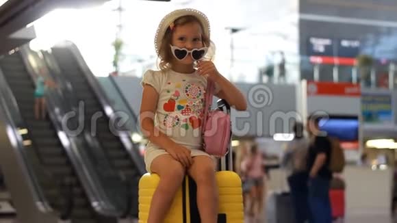 小女孩游客坐在火车站的一个大黄色手提箱上儿童正在等待出发前往视频的预览图