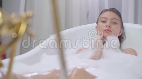 美丽的女人躺在浴缸里泡澡放松在有泡沫泡浴的浴缸里轻松愉快地躺着视频的预览图