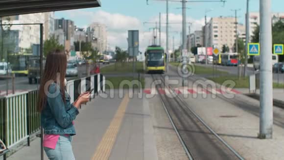 穿着蓝色外套的年轻女子在户外车站等电车视频的预览图