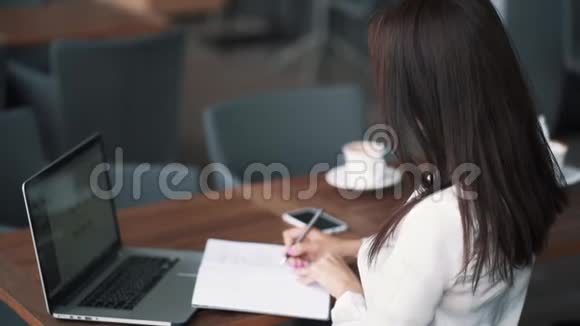 女商人在咖啡馆工作在笔记本上写笔记慢动作视频的预览图