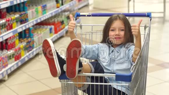 一个滑稽的小女孩坐在超市的购物车里伸出大拇指视频的预览图