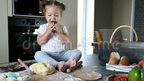 小女孩穿着白色T恤坐在厨房的桌子上视频的预览图