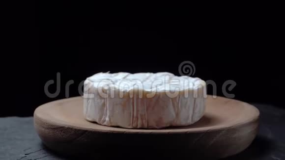 卡门伯特奶酪在深色背景下的木盘上旋转视频的预览图