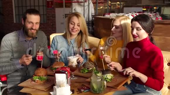四个快乐的朋友在一家有刀叉的咖啡馆里玩得很开心他们吃汉堡视频的预览图