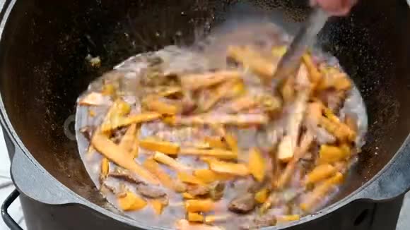 在铸铁大锅里做饭带肉的胡萝卜用热油炸用大金属勺子搅拌配料视频的预览图