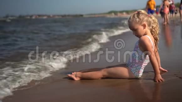 可爱的小女孩坐在海岸线上在岸上遇到海浪儿童逃跑视频的预览图