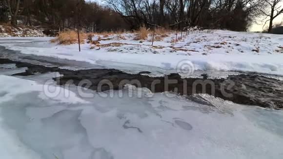随着小溪的水流在冰覆盖的河岸之间平稳地流动视频的预览图