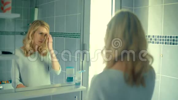 女人在浴室里对着镜子系着她的金发视频的预览图